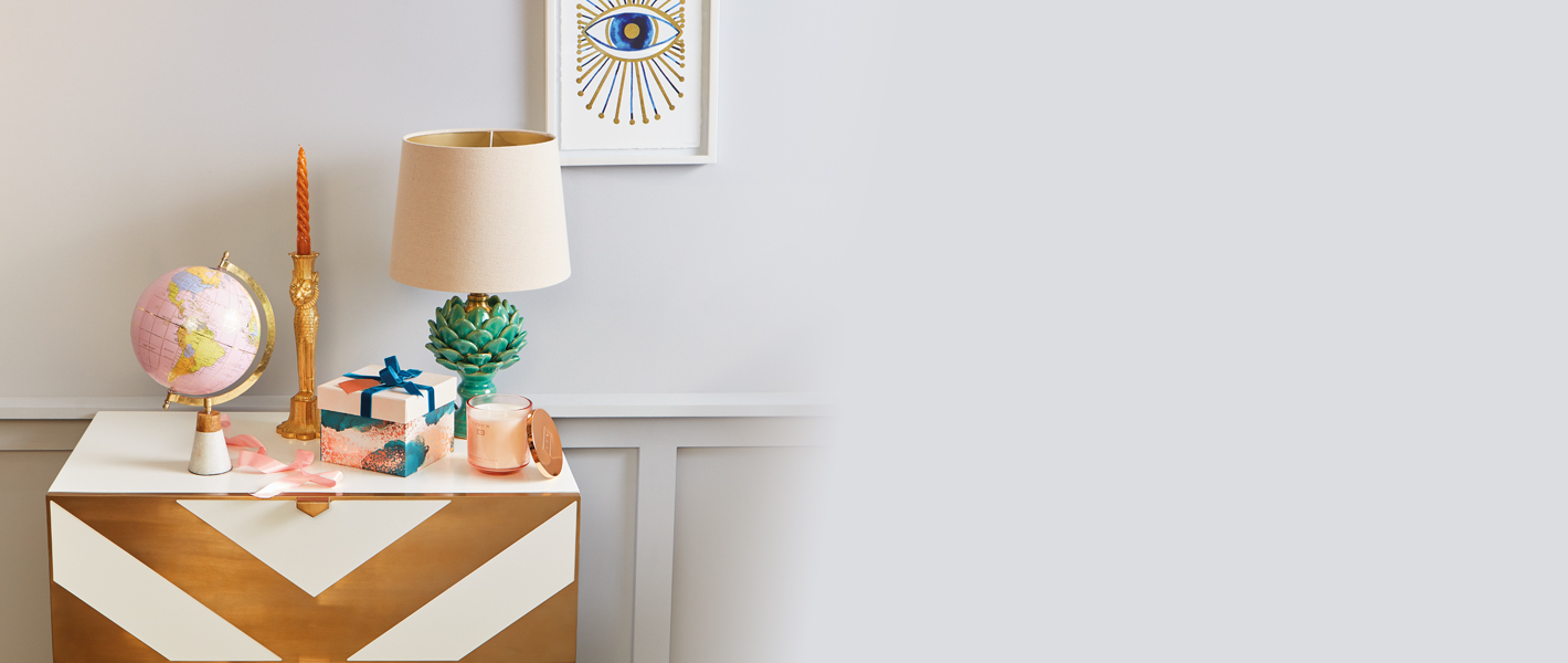 Decorative chest with lamp, globe, candle, gift box, and framed artwork.