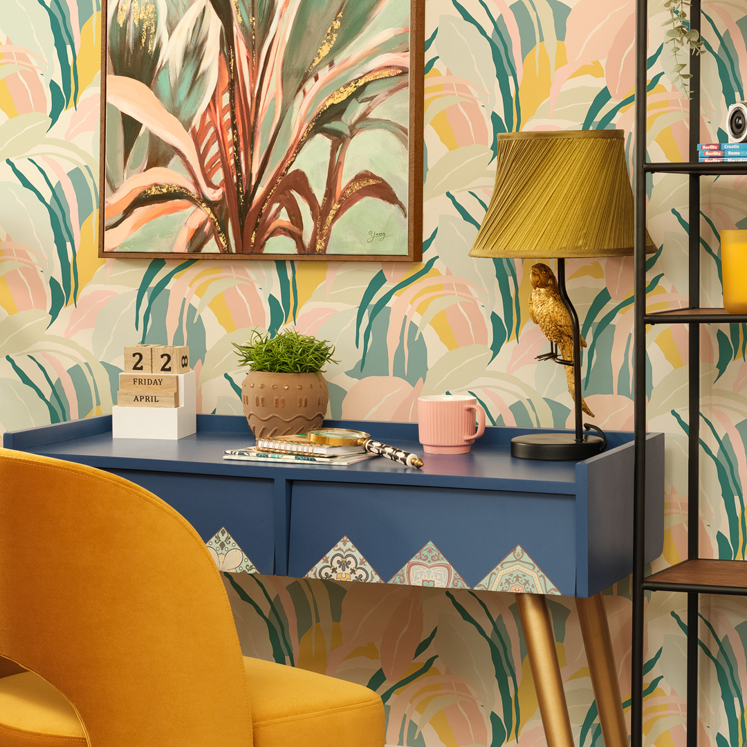 Colorful home office setup with blue desk, yellow chair, table lamp, plant, and wall art.