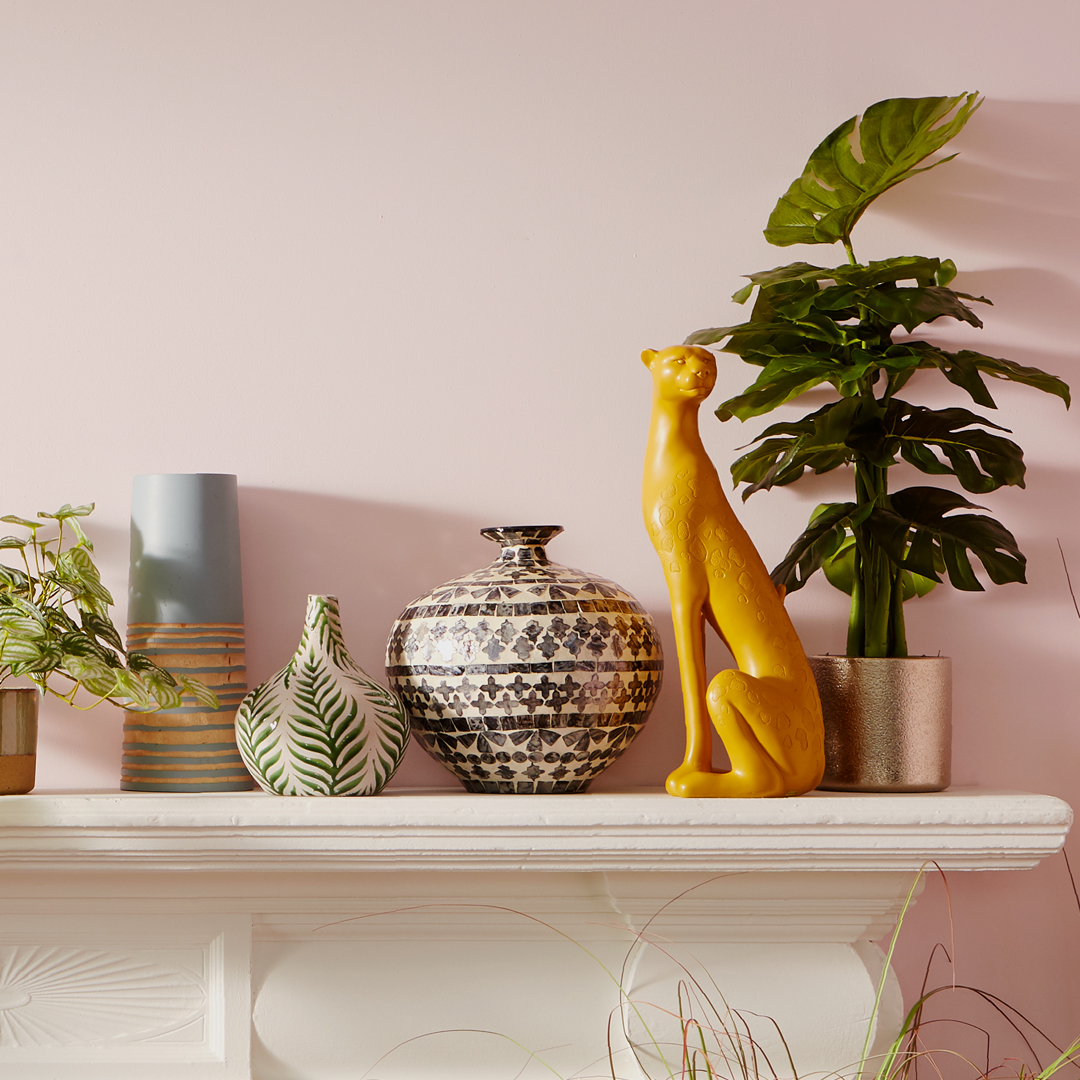 A stylish mantel with decorative vases, plants, and a yellow animal statue.