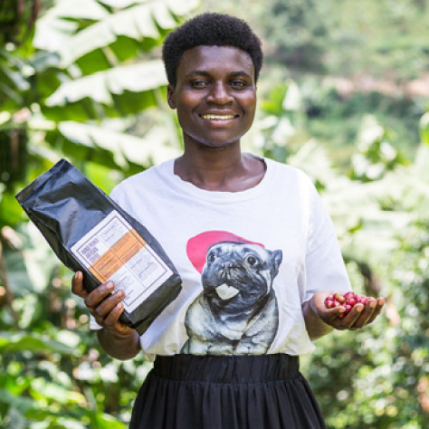 A person holding a packet of coffee and a handful of coffee cherries, smiling in a lush green environment.