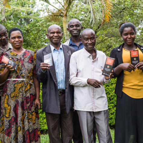A group of six people standing together, smiling and holding packets of coffee in an outdoor setting.
