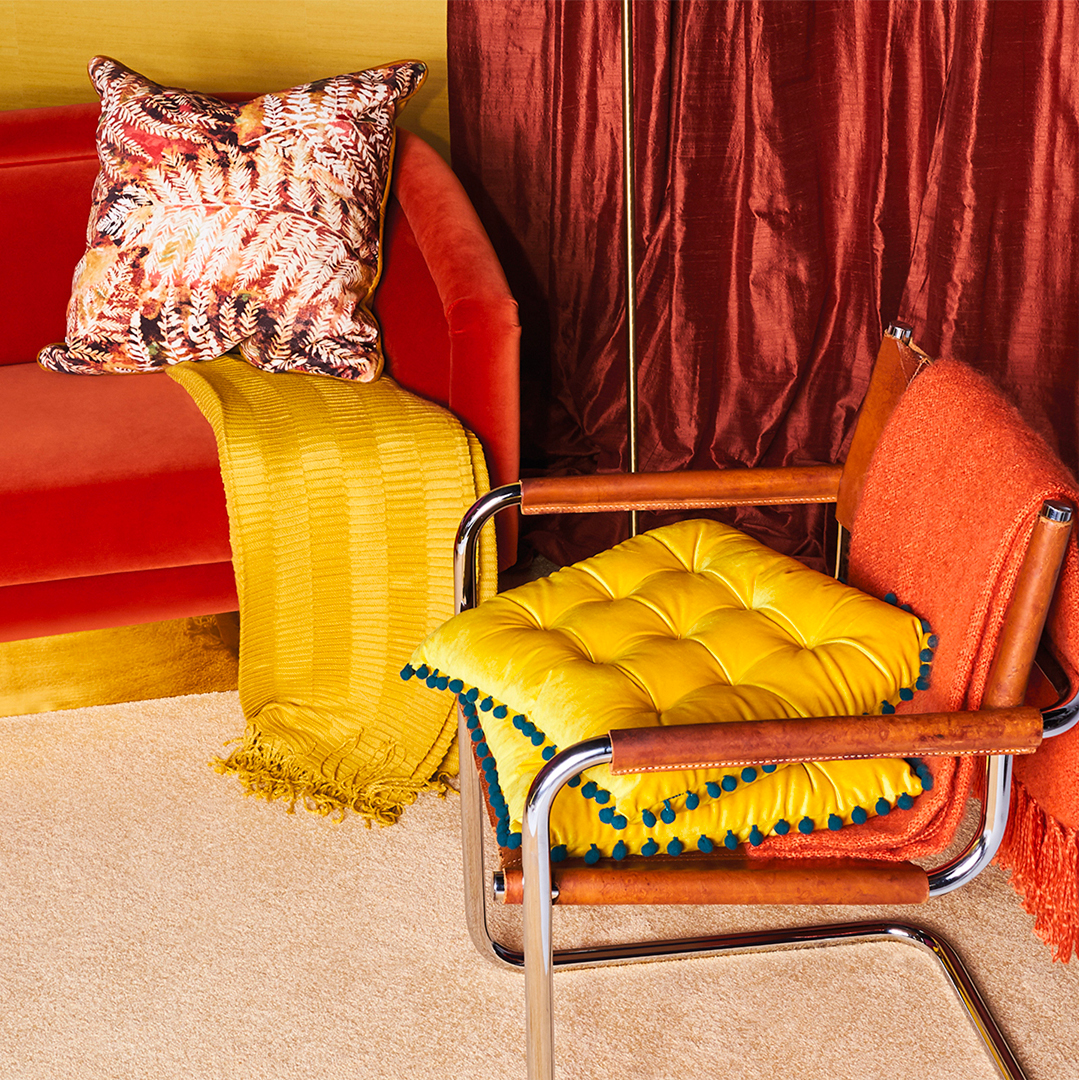 Cozy space with a red sofa, yellow throw, and a chair stacked with bright yellow cushions and an orange blanket.