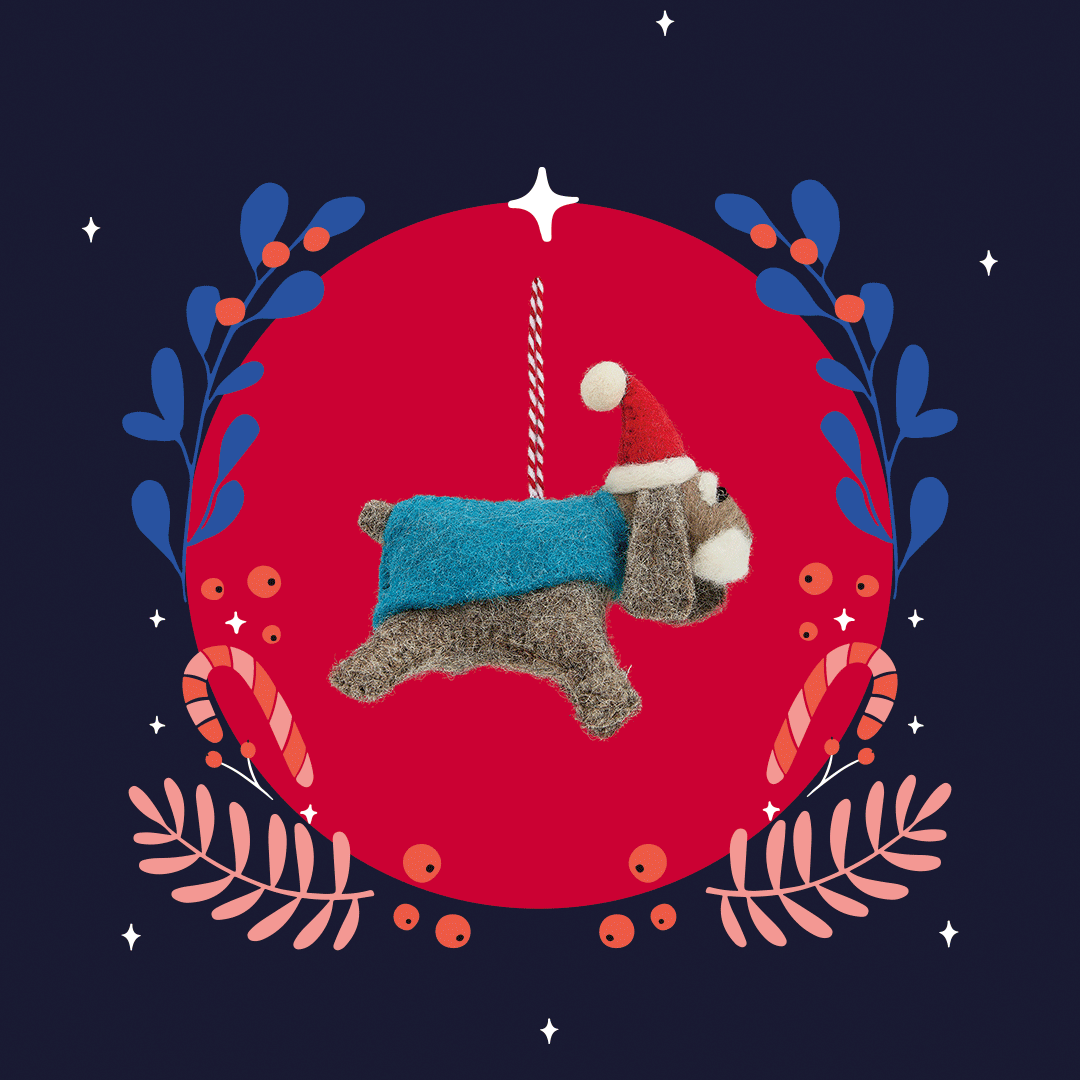 A festive handmade ornament of a dog wearing a red Santa hat and a blue sweater, hanging from a string. The ornament is set against a red background with holiday-themed decorations like foliage and candy canes.