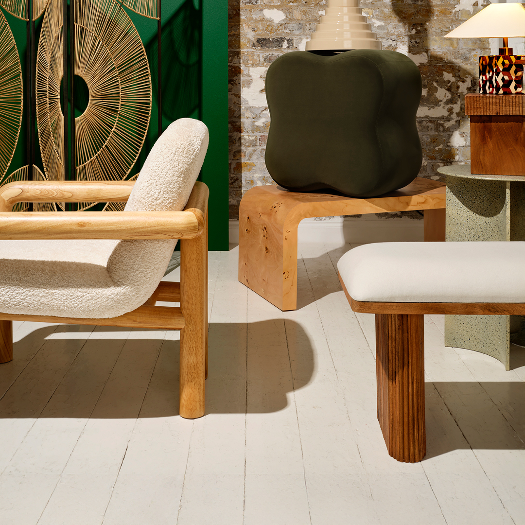 Modern living room interior with wooden furniture, cream upholstered chairs, a sculptural green side table, and decorative lamps against a brick and green accent wall.