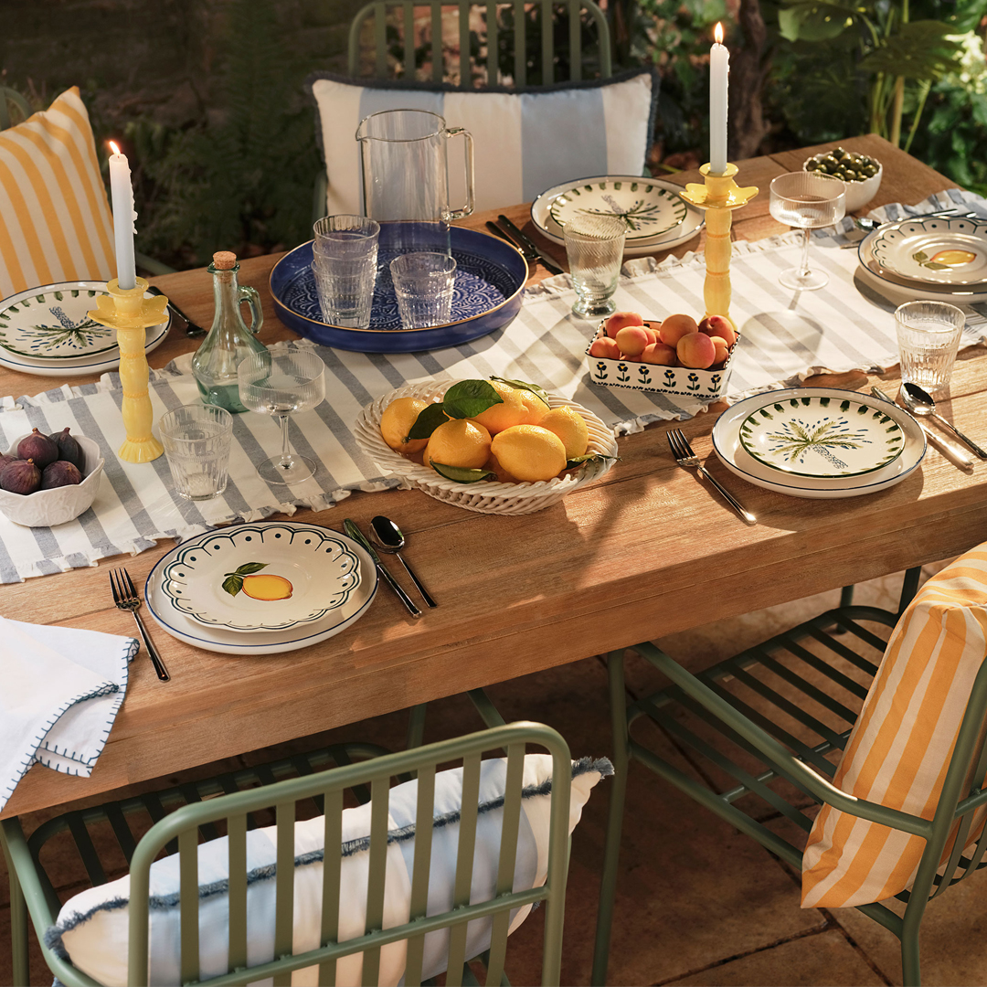 Outdoor table set for a meal with fruit-themed plates and fresh produce.