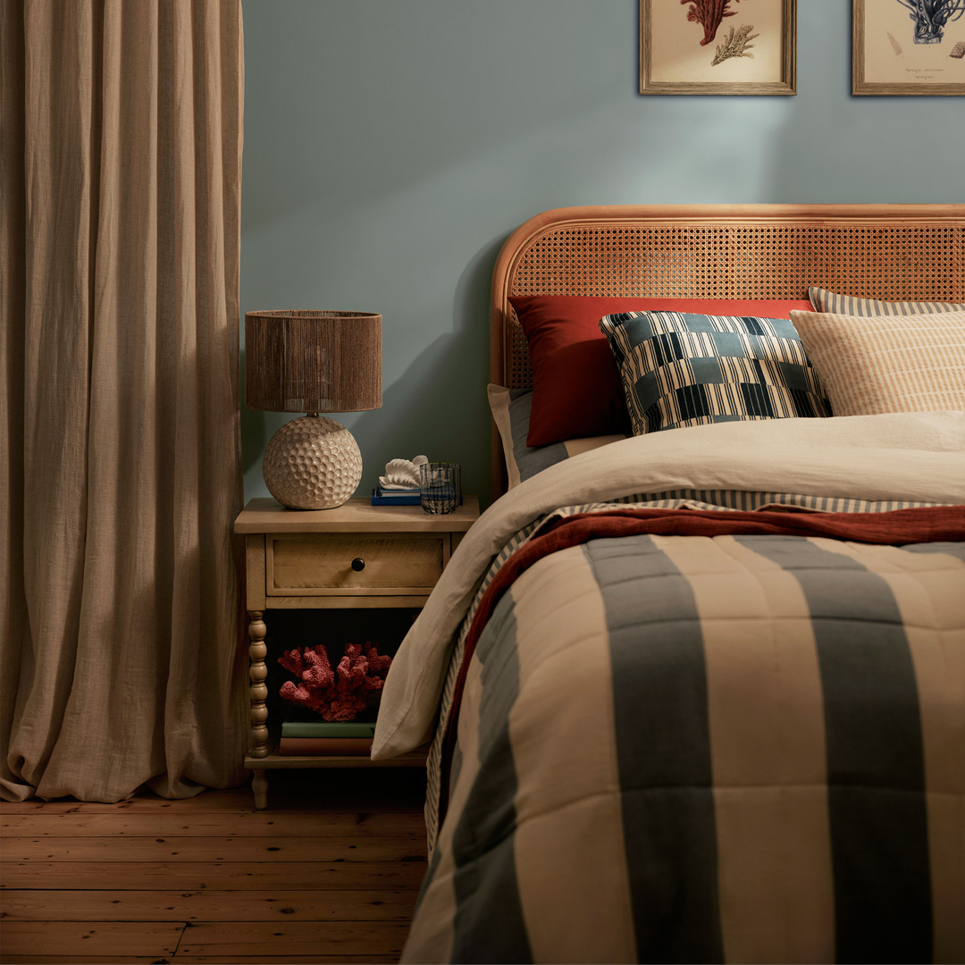 Cozy bedroom with a striped bedspread, rattan headboard, and bedside table with a lamp.