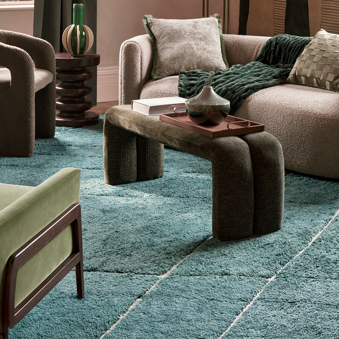 Cozy living room with a beige sofa, green throw, green chair, and teal rug.