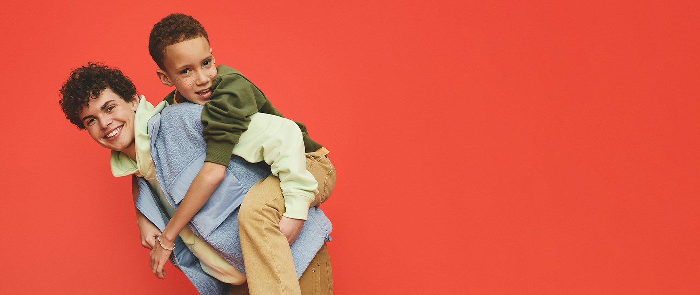 An older boy carries a younger boy on his back, both are smiling and looking towards the camera.