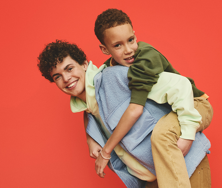 An older boy carries a younger boy on his back, both are smiling and looking towards the camera.